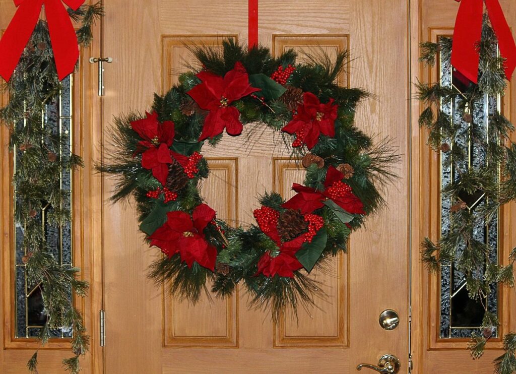 A holiday wreath with red poinsettias and pine cones on a wooden front door